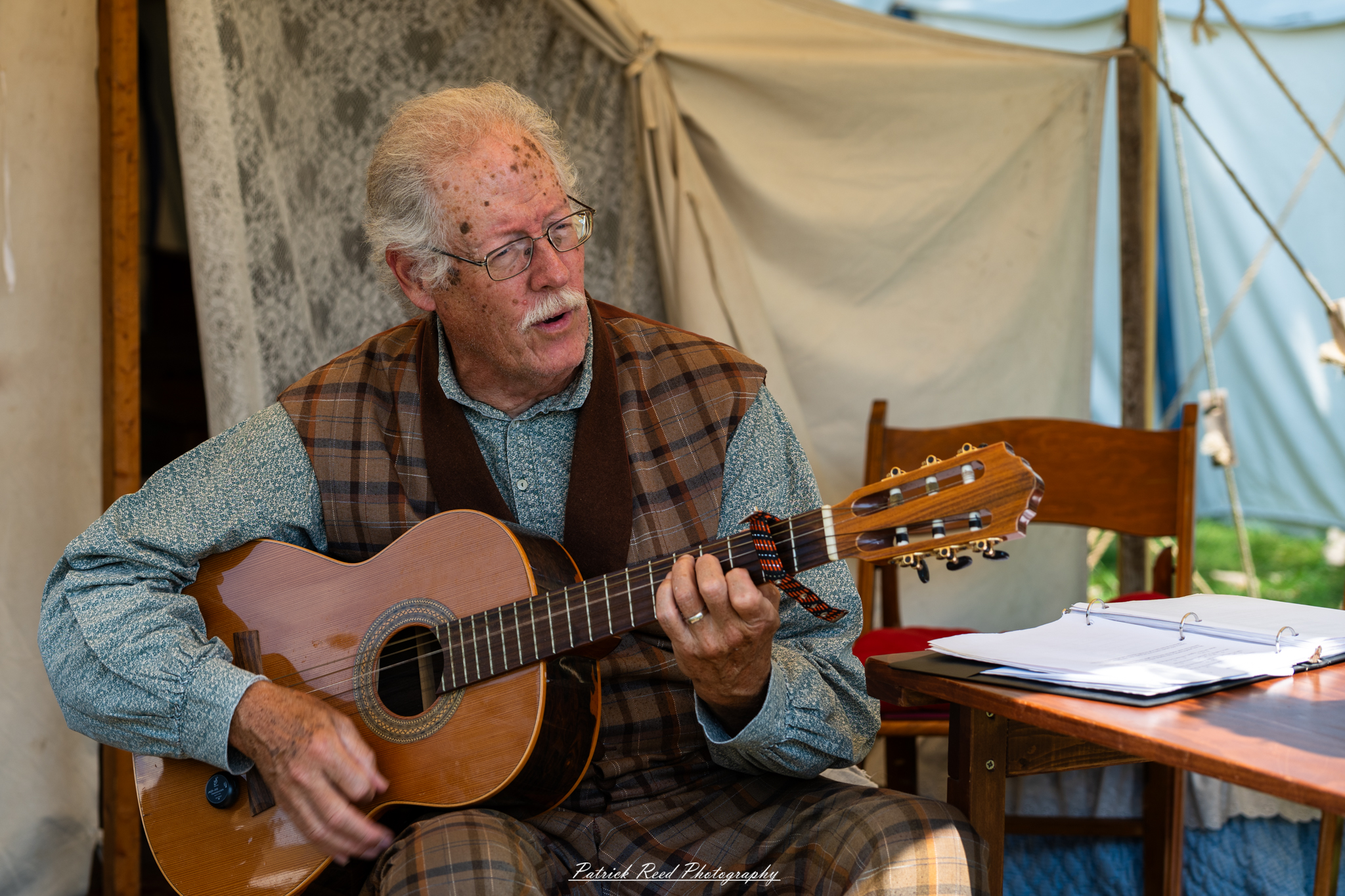 A man playing guitar while dressed in period clothing, showcasing the style of a bygone era. His attire features authentic details, such as a waistcoat and trousers, and he strums the guitar with passion, creating an atmosphere of nostalgia and musical enjoyment in a historical setting.